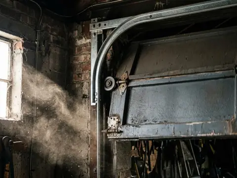 Upper corner of a moving garage door with hinges, rollers and track lit by a dusty beam of light
